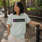 Person wearing a Bay-colored Comfort Colors t-shirt with 'Flushing-Main St' design, standing outdoors.