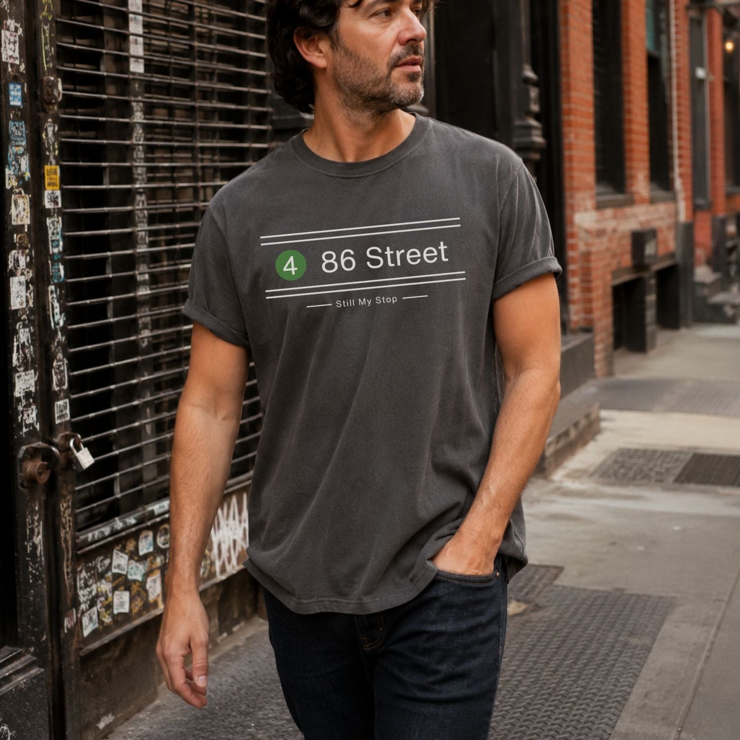 Man wearing a Dark gray t-shirt with '86 Street' printed on it, standing on a city street.