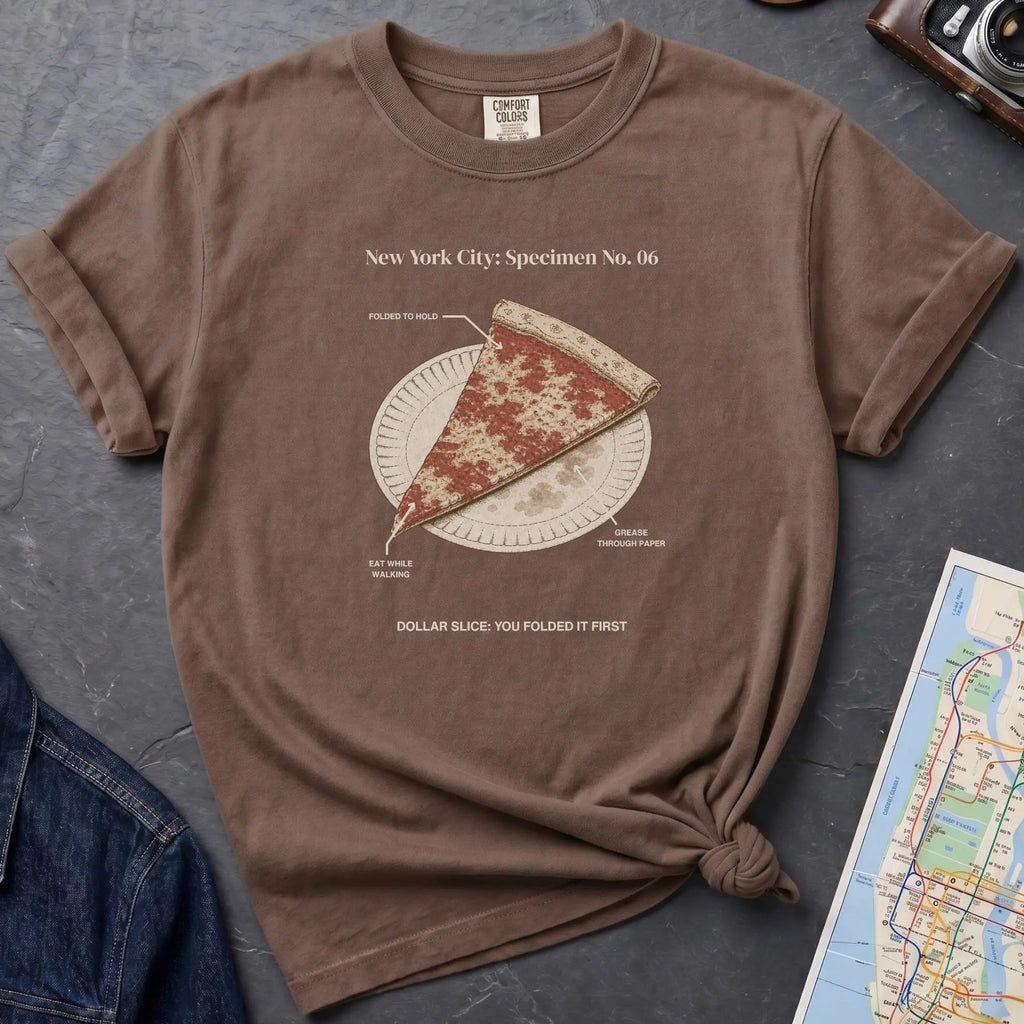 Brown Comfort Colors t-shirt featuring a vintage New York City dollar slice pizza graphic with specimen-style callouts and a folded slice on a paper plate.