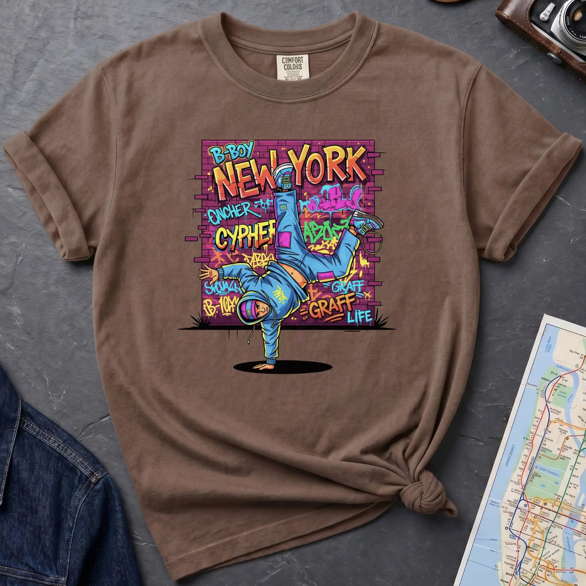 Brown Comfort Colors t-shirt featuring a colorful B-Boy New York graphic with a breakdancer in front of a graffiti brick wall.