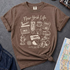 Brown Comfort Colors t-shirt featuring a New York Life Was the Best Life graphic with hand-drawn NYC nostalgia icons including a MetroCard, cassette tape, pay phone, coffee cup, newspaper, pizza slice, fire hydrant, Walkman, and bodega cat.