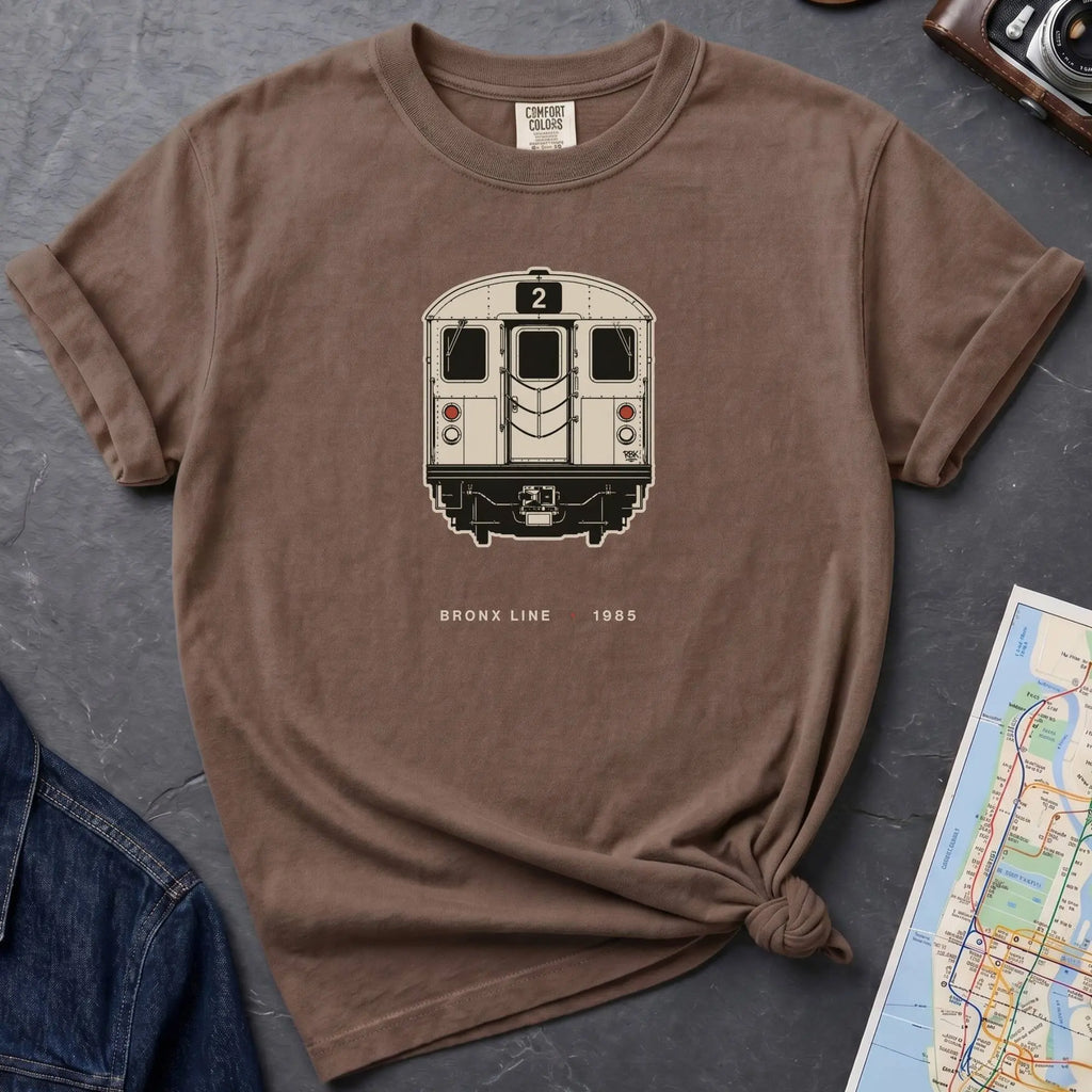 Brown t-shirt with a NYC subway train graphic on a dark surface with a map and a denim jacket.