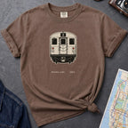 Brown t-shirt with a NYC subway train graphic on a dark surface with a map and a denim jacket.