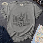 Granite colored t-shirt with a Golden Doodle dog and cityscape design on a gray surface with a map and camera.