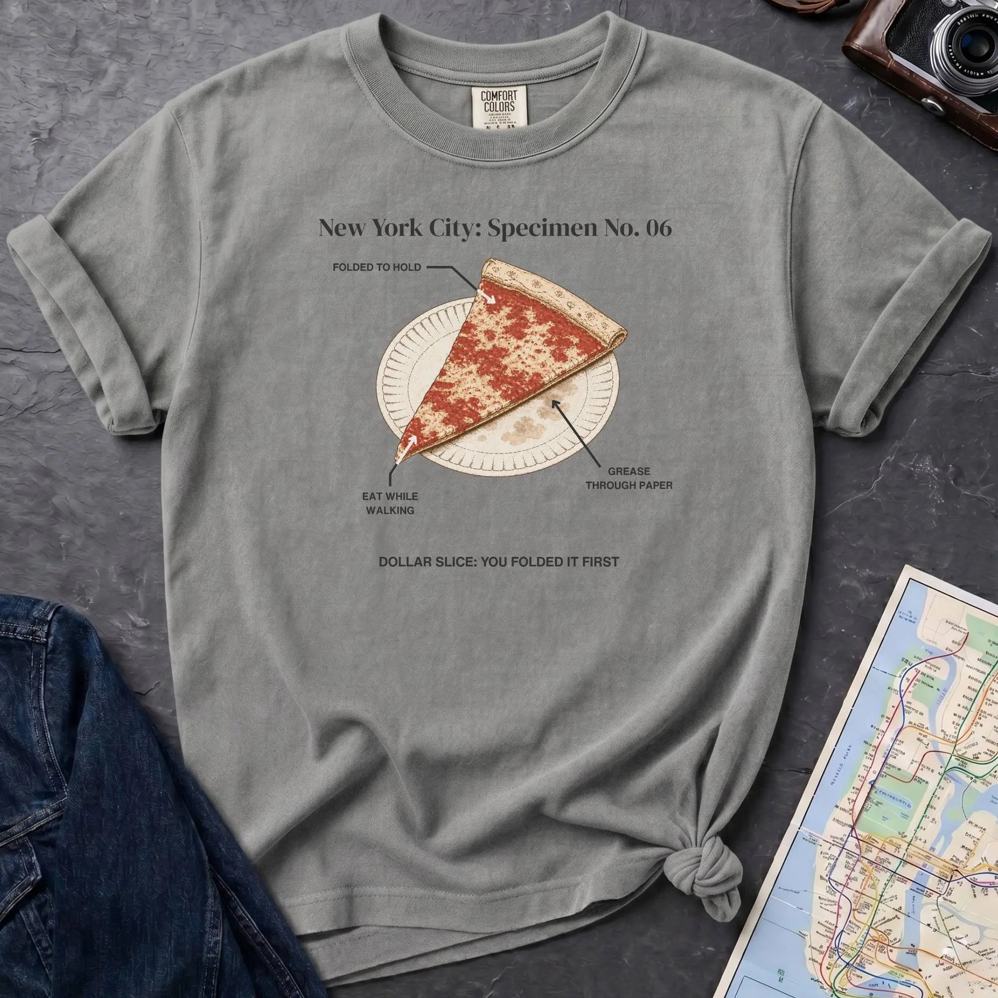 Granite colored Comfort Colors t-shirt featuring a vintage New York City dollar slice pizza graphic with specimen-style callouts and a folded slice on a paper plate.