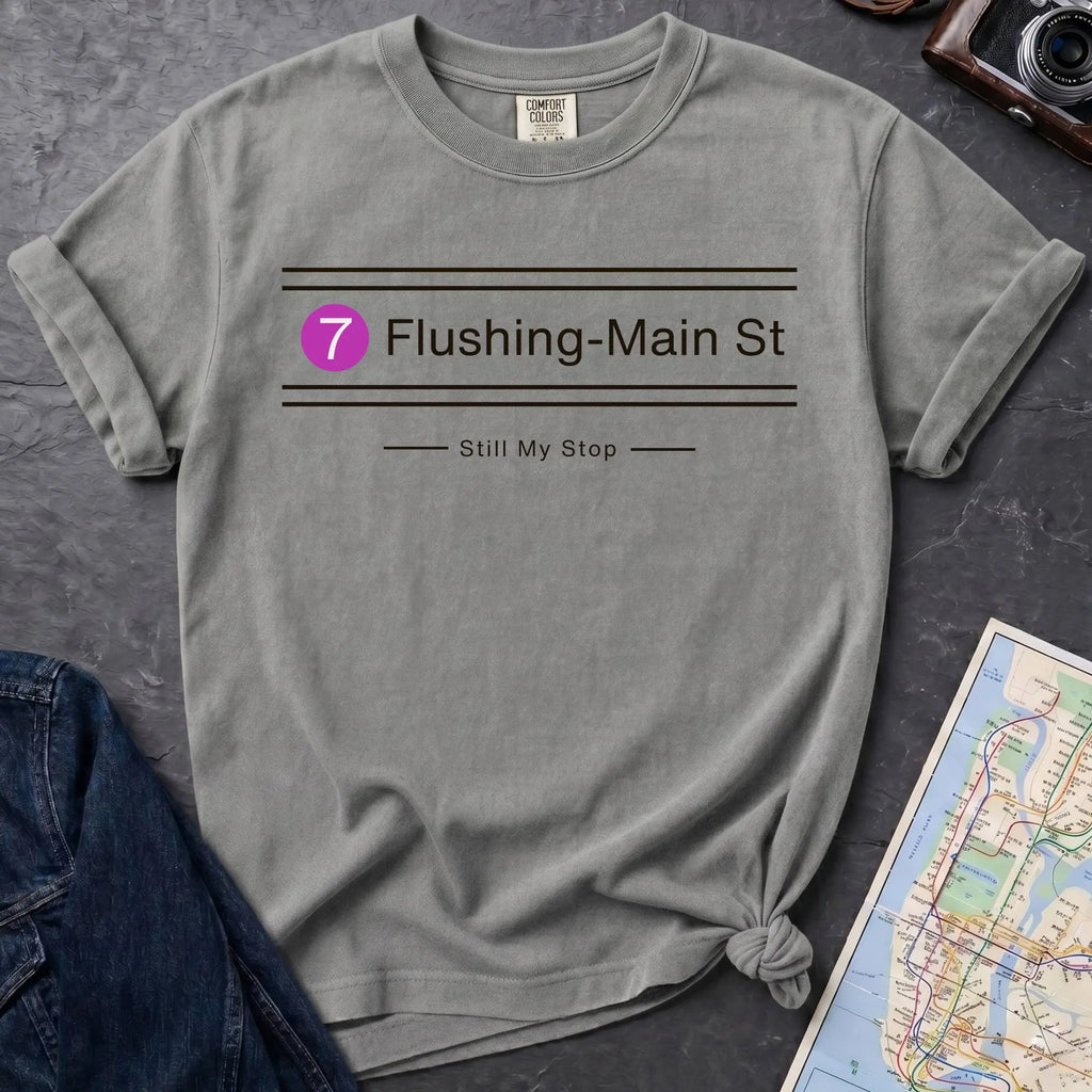 Granite colored t-shirt with 'Flushing-Main St' design on a dark surface with a denim jacket and a map.
