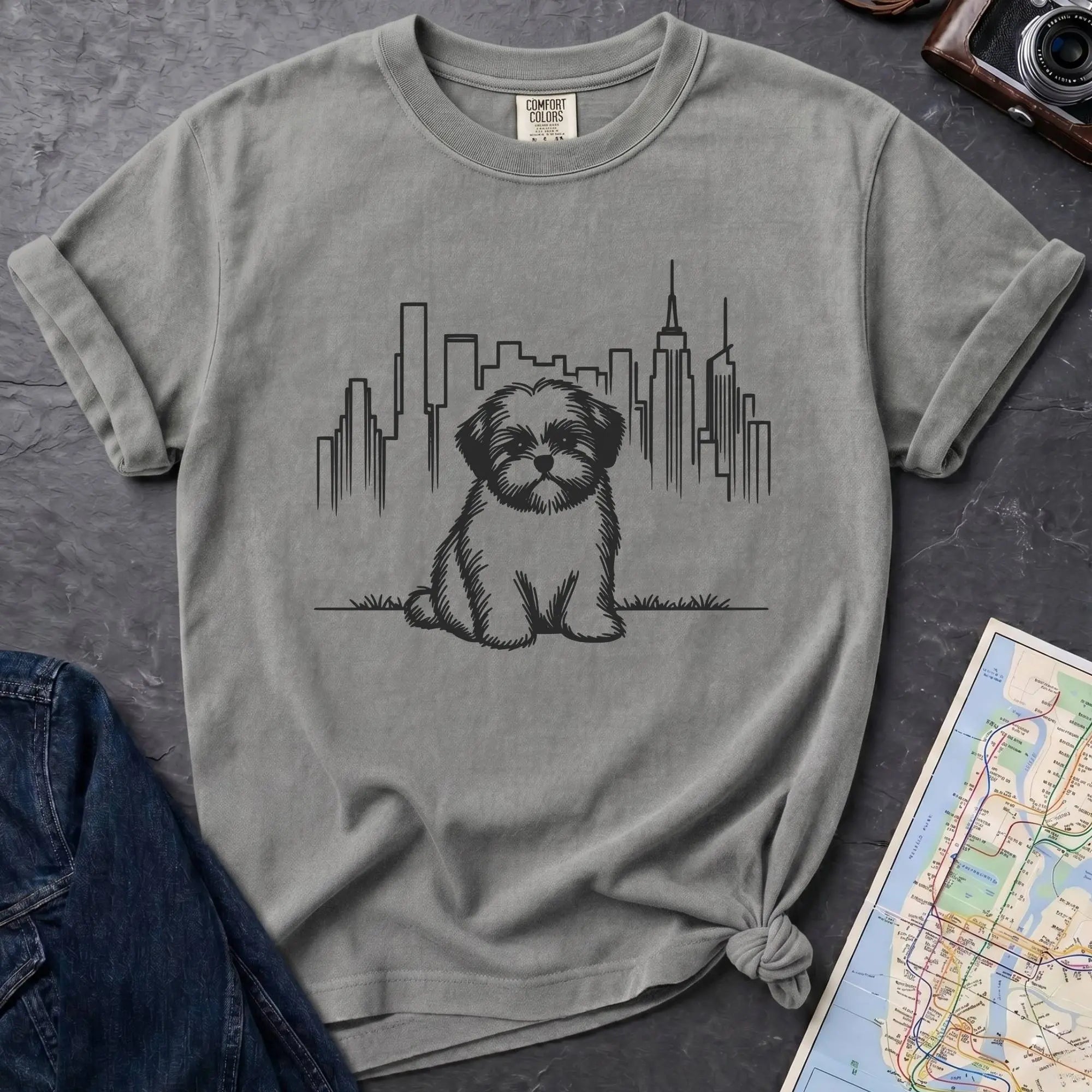 Granite colored t-shirt with a Shih Tzu dog and cityscape design on a dark surface with a map and camera.