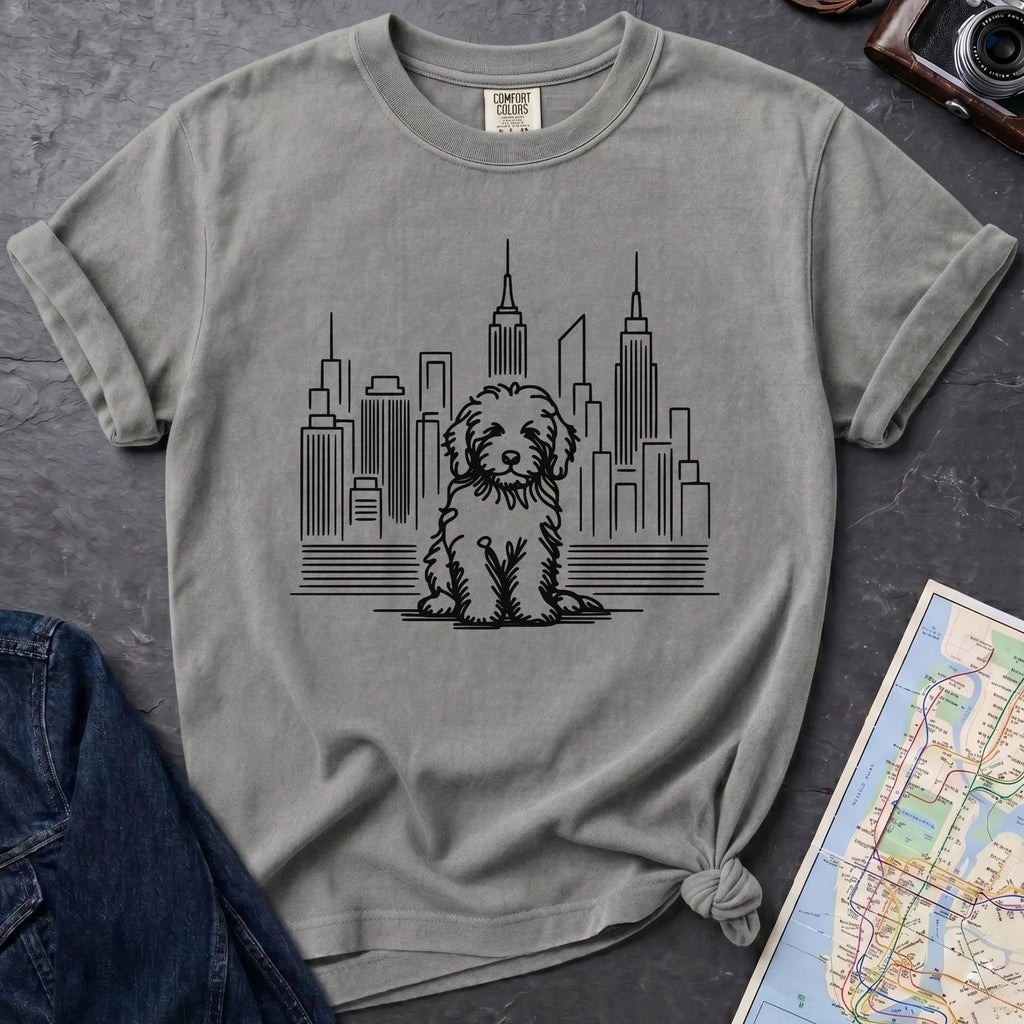 Granite colored t-shirt with a Golden Doodle dog and cityscape design on a gray surface with a map and camera.