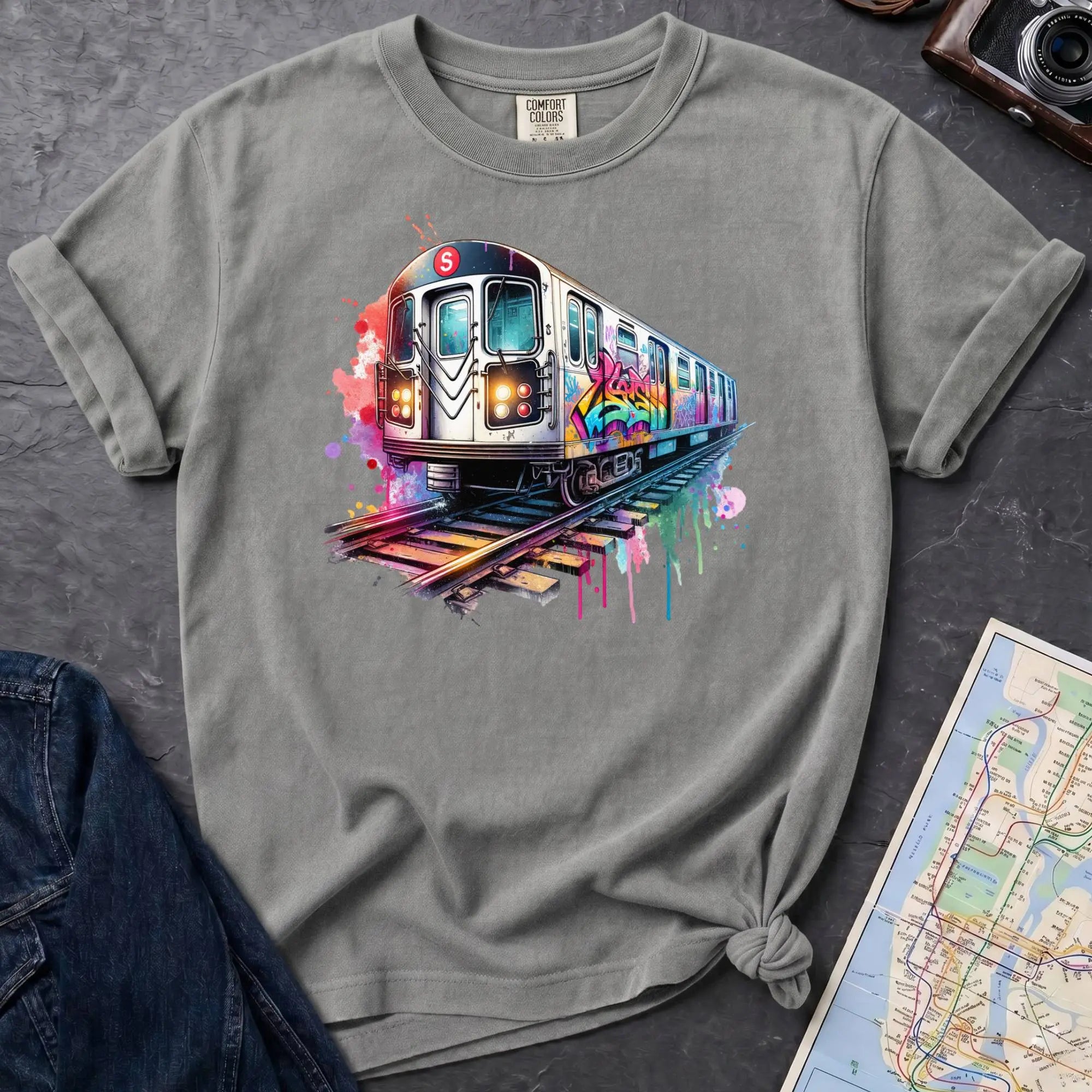Granite colored Comfort Colors t-shirt featuring a colorful NYC subway train graphic with graffiti-style paint details and bright street art accents.