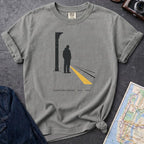 Granite colored t-shirt with a graphic design of a person on a train platform, placed on a dark surface with a map and denim jacket.