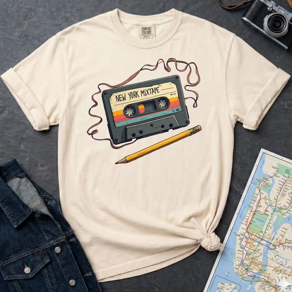 Ivory t-shirt with a cassette tape graphic and pencil on a gray surface with a map and denim jacket.