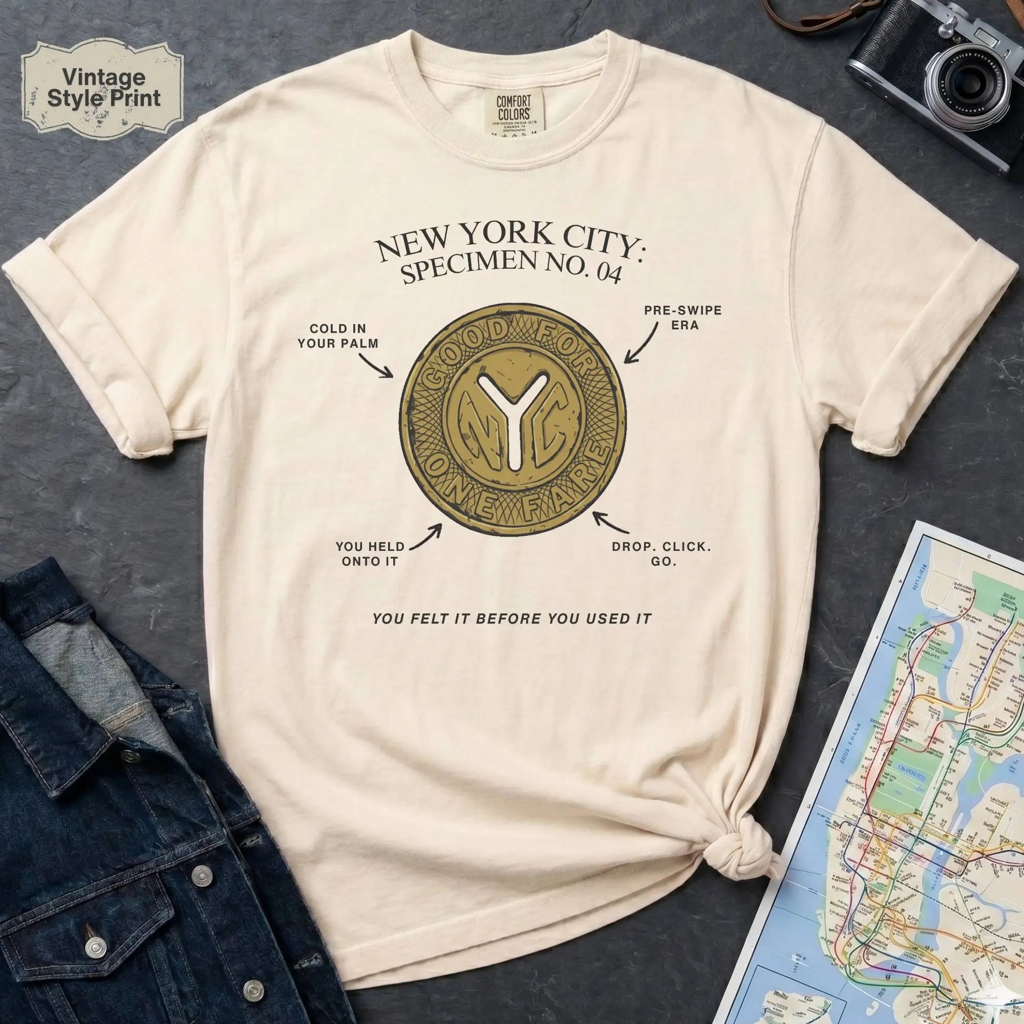 Ivory Comfort Colors t-shirt featuring a vintage New York City subway token graphic with specimen-style callouts and “You felt it before you used it” text.