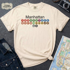 Ivory Comfort Colors t-shirt featuring a minimalist Manhattan subway line graphic with colorful NYC train icons.