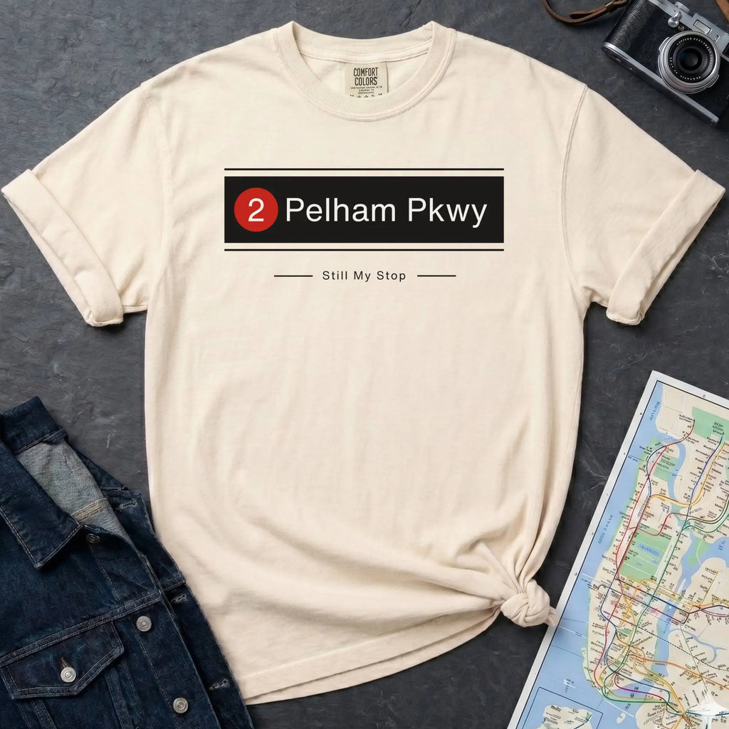 Ivory t-shirt with '2 Pelham Pkwy Still My Stop' design on a dark surface with denim jacket and map.