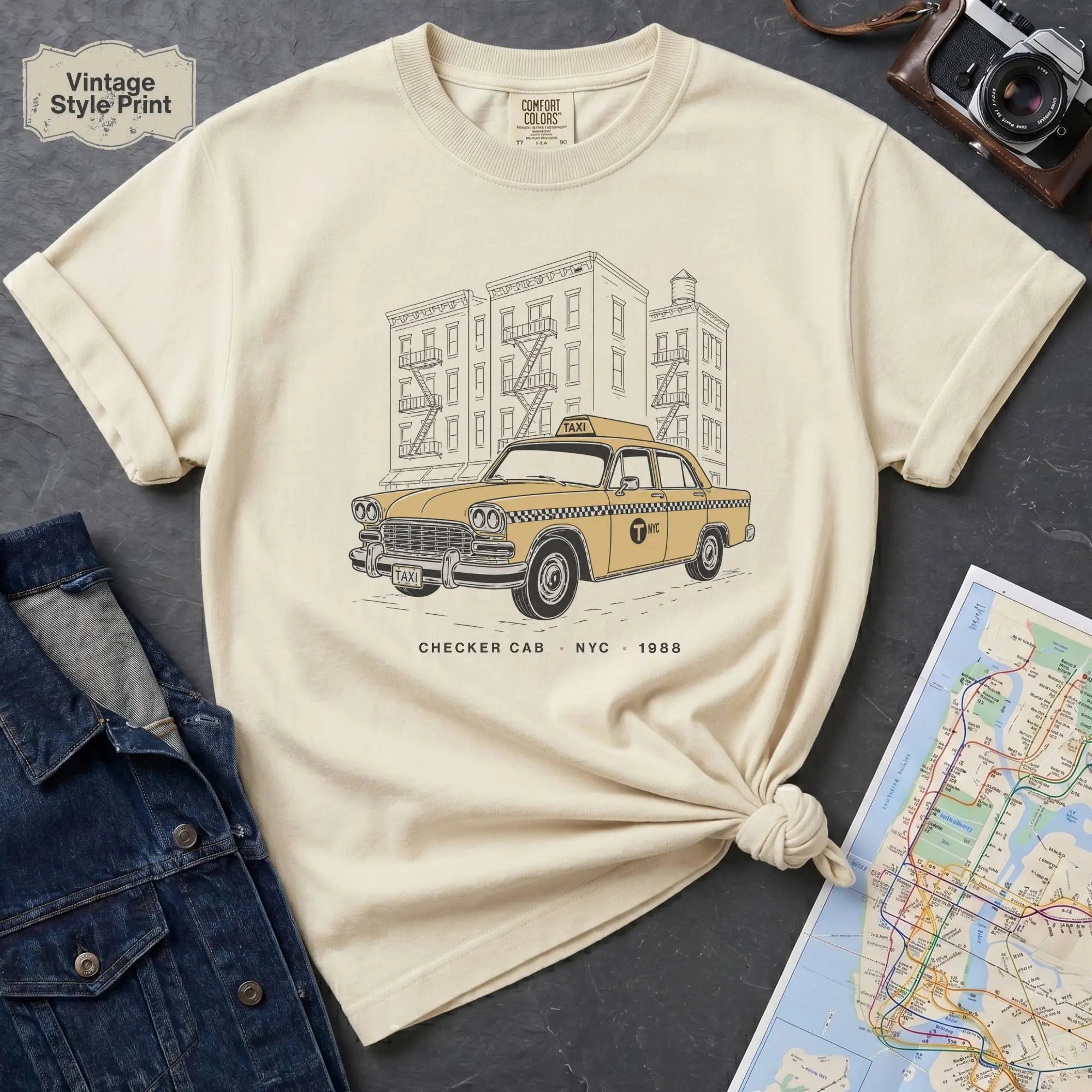 Ivory Comfort Colors t-shirt featuring a vintage New York City Checker Cab graphic with NYC apartment buildings and “Checker Cab • NYC • 1988” text.