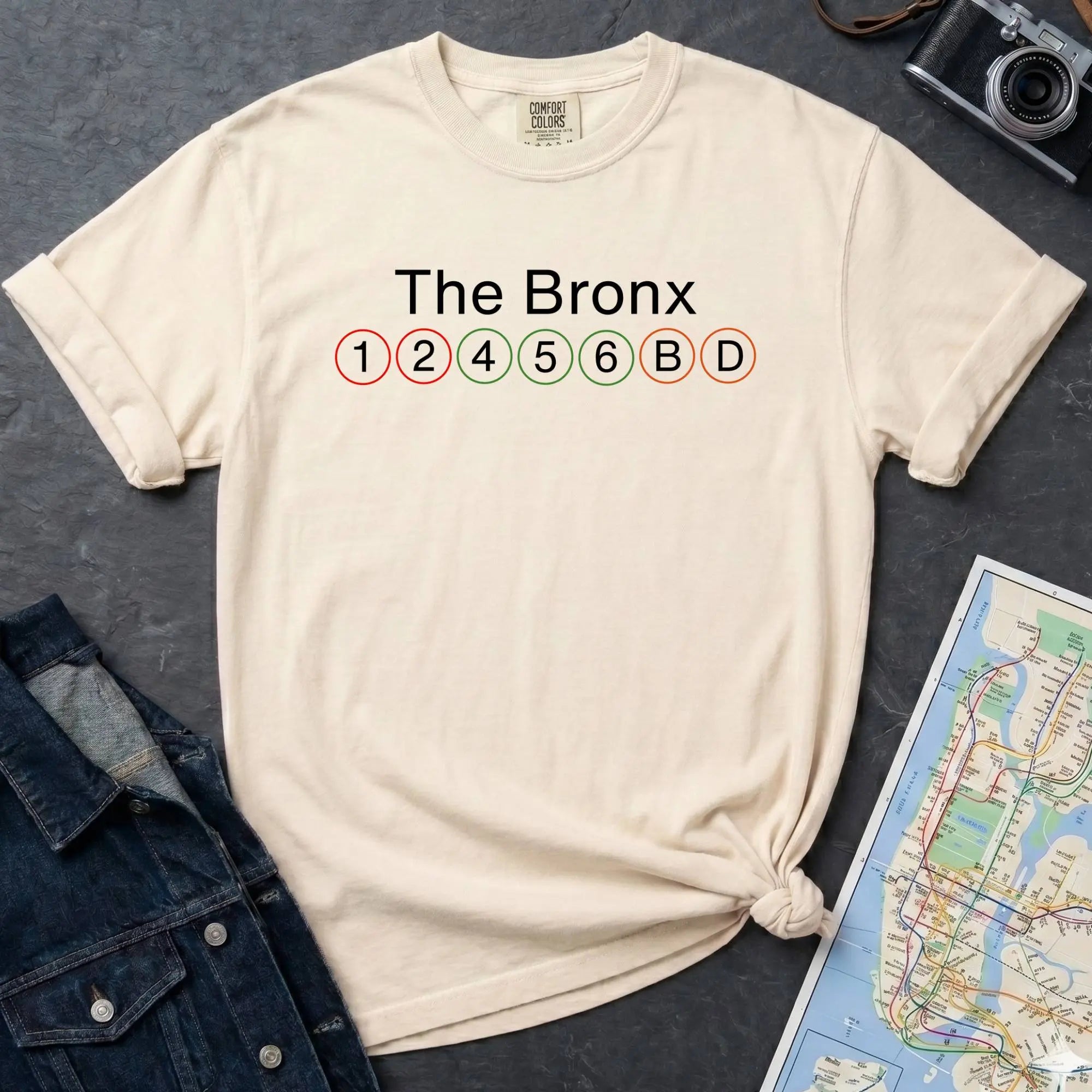 Ivory Comfort Colors t-shirt featuring a minimalist Bronx subway line graphic with The Bronx text and classic NYC train icons.