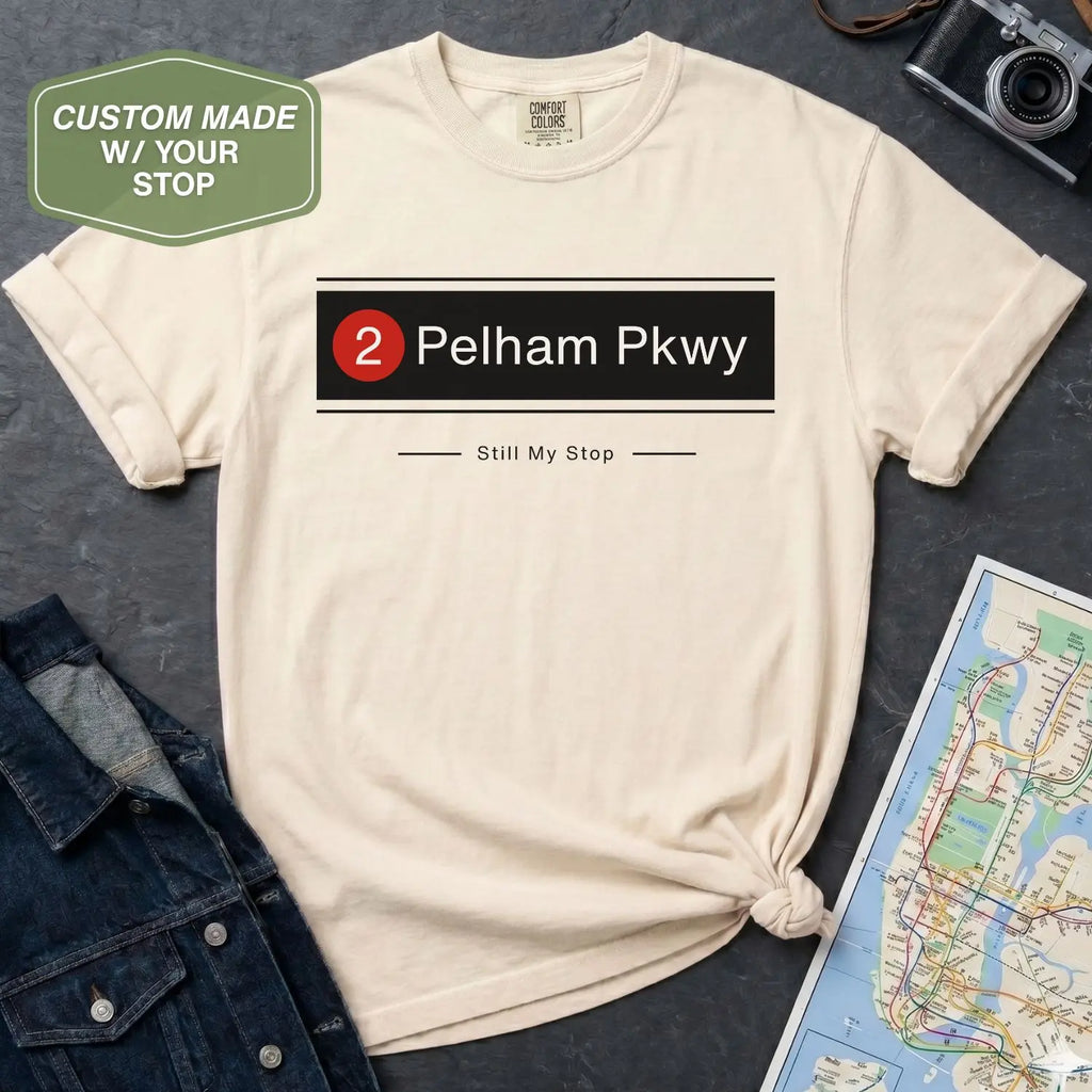 Ivory Comfort Colors t-shirt with '2 Pelham Pkwy' and 'Still My Stop' text design on a dark surface with denim jacket and map.
