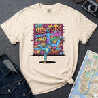 Ivory t-shirt with a colorful graphic design featuring a breakdancer and text on a dark surface with a denim jacket and a map.