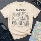 Ivory Comfort Colors t-shirt featuring an 80’s NYC Kid Starter Pack graphic with hand-drawn New York City icons including Italian ice, a radio, stoop steps, stickball, a fire hydrant, and a pigeon.