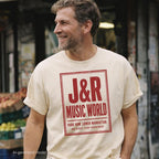 Man wearing an ivory Comfort Colors T-shirt with red J&R Music World NYC front print, while standing in front of a bodega in New York. 