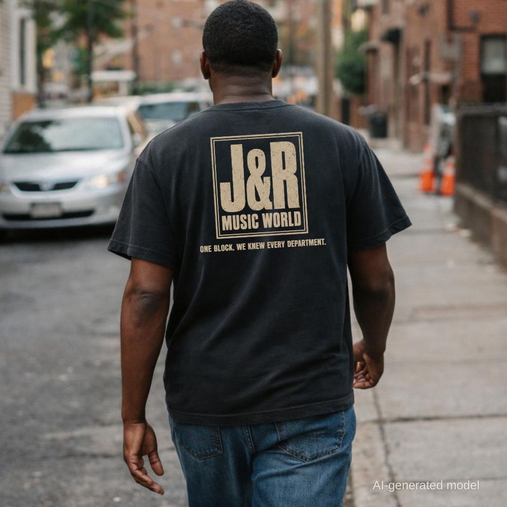 A man wearing a black Comfort Colors T-shirt with off-white J&R Music World NYC back print, while walking down a city street.