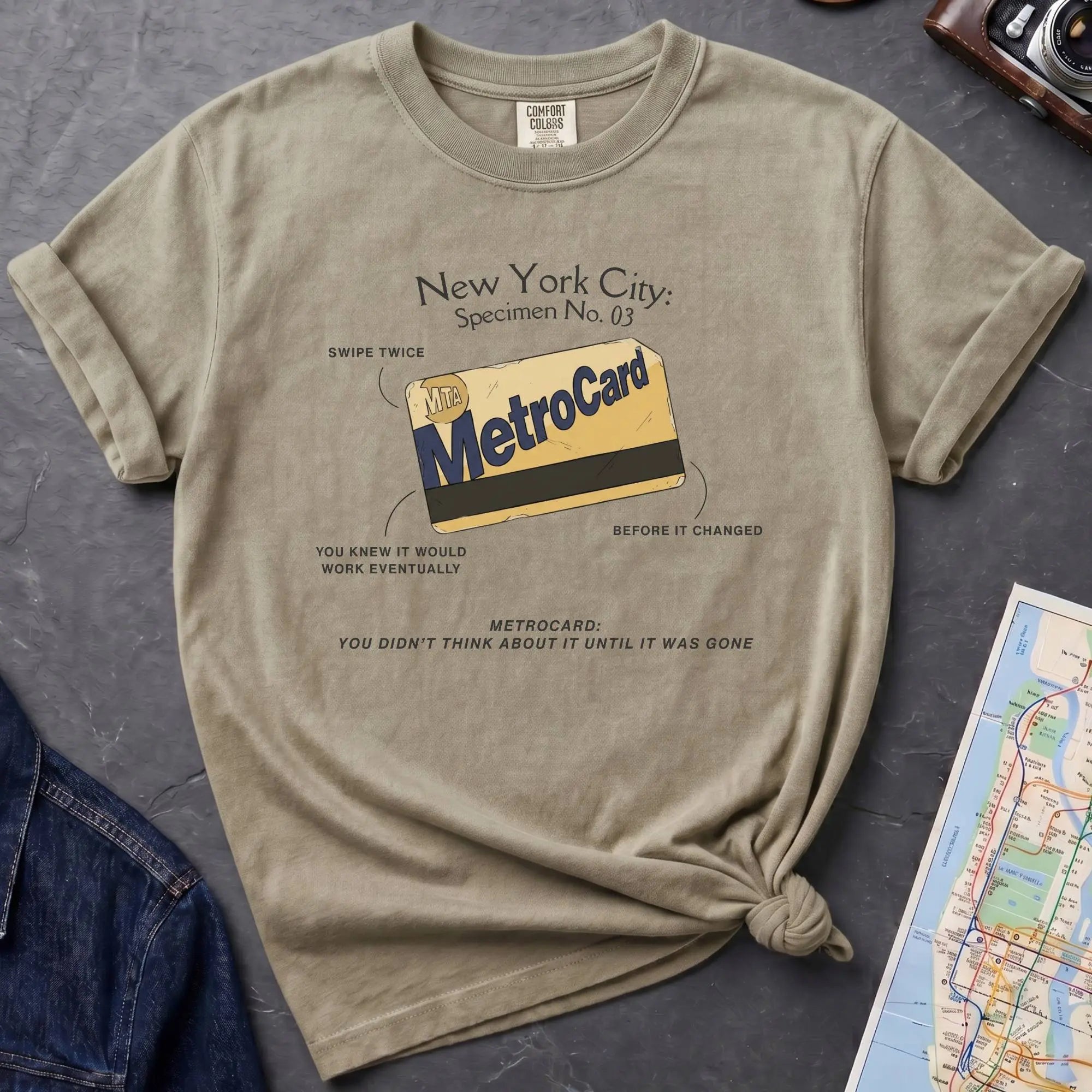Khaki colored Comfort Colors t-shirt featuring a vintage New York City MetroCard graphic with specimen-style callouts and “You didn’t think about it until it was gone” text.