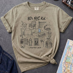 Khaki colored Comfort Colors t-shirt featuring an 80’s NYC Kid Starter Pack graphic with hand-drawn New York City icons including Italian ice, a radio, stoop steps, stickball, a fire hydrant, and a pigeon.