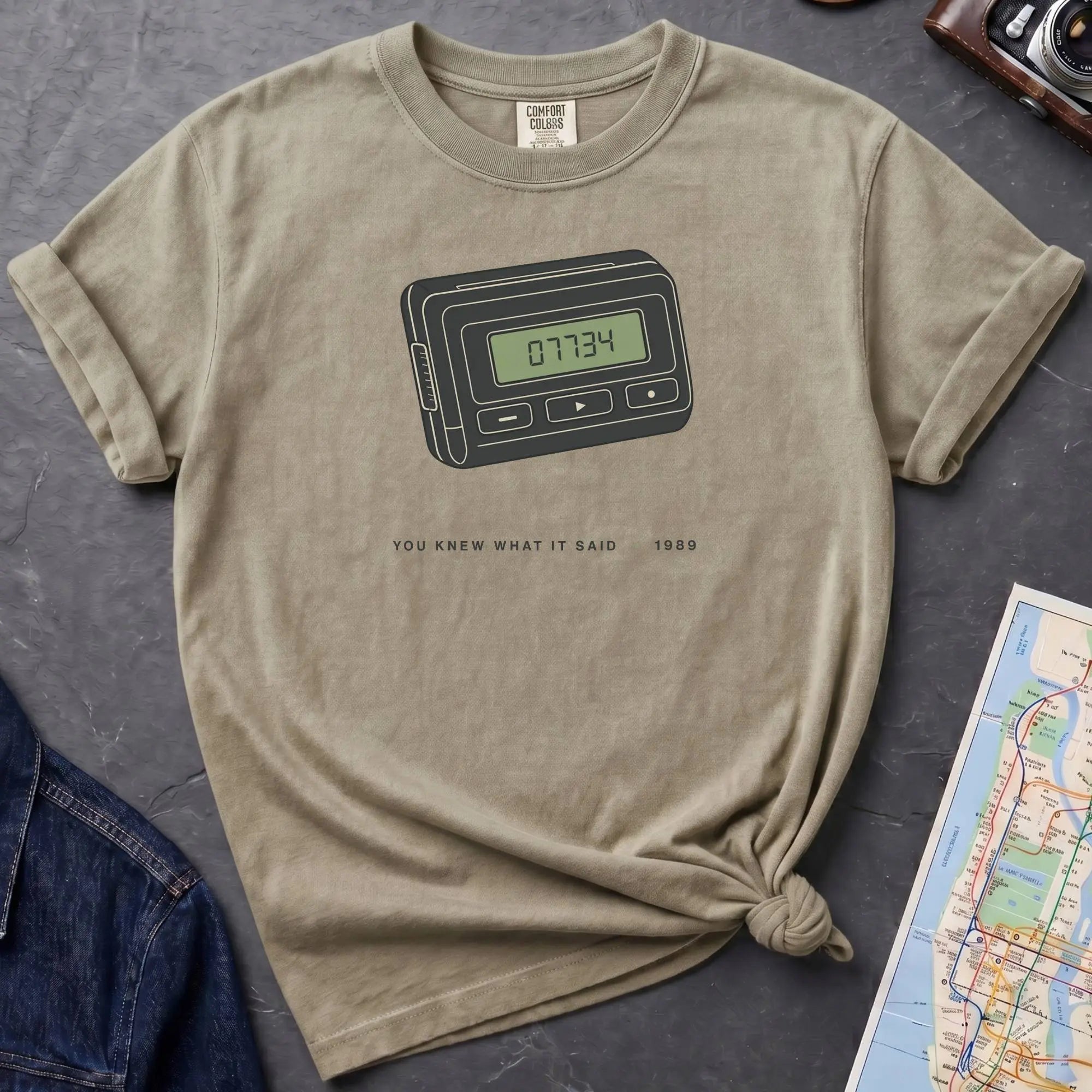 Khaki colored Comfort Colors t-shirt featuring a retro pager graphic with “07734” on the screen and “You knew what it said • 1989” text.