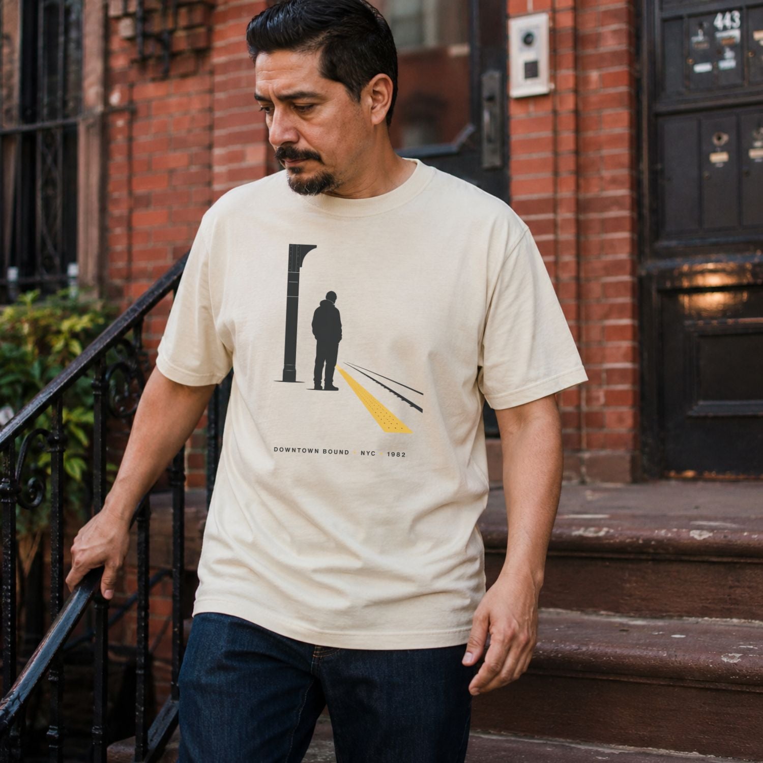 Man wearing a Ivory Comfort Colors t-shirt with a graphic design of a train station platform, standing on a street.