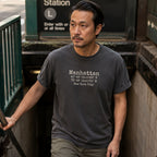 Man wearing a Pepper colored Comfort Colors t-shirt with Manhattan coordinates in a subway station
