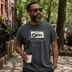 Man wearing a Pepper colored Comfort Colors t-shirt with a cassette tape design, standing on a street