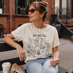 Woman wearing an Ivory Comfort Colors t-shirt with '80's NYC Kid' graphic design sitting outdoors.