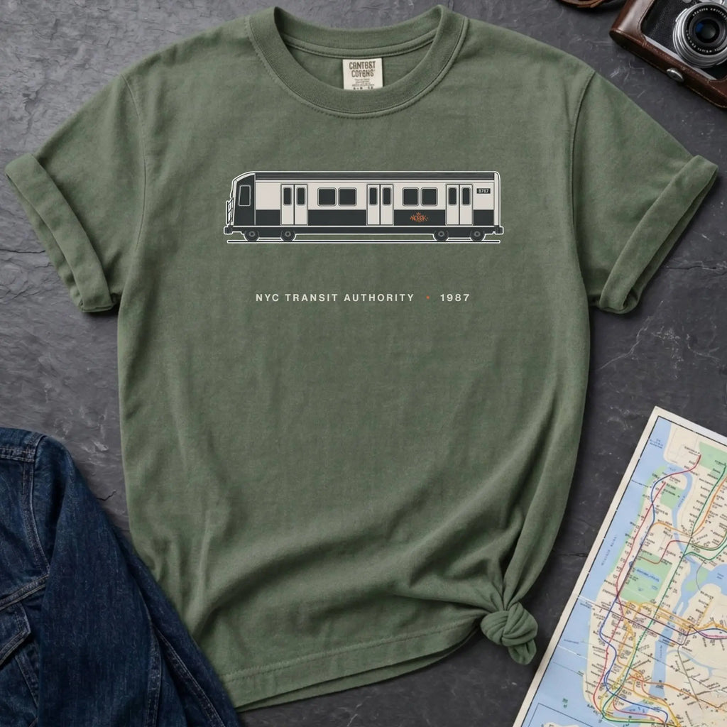 Moss green Comfort Colors t-shirt featuring a minimalist New York City subway car graphic with “NYC Transit Authority • 1987” text.