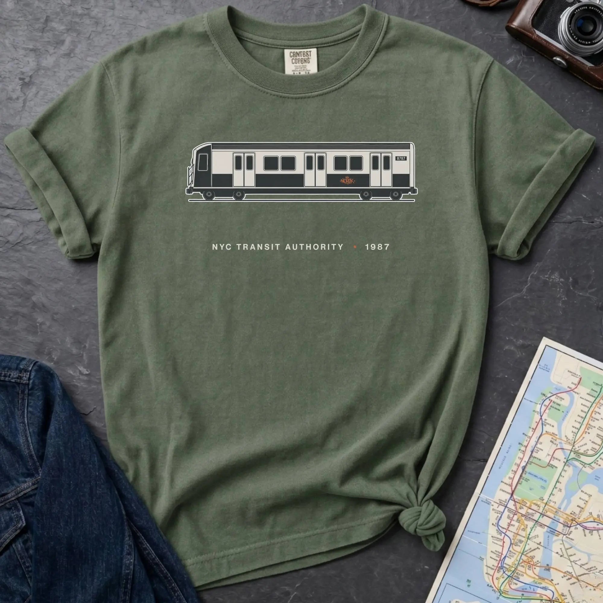 Moss green Comfort Colors t-shirt featuring a minimalist New York City subway car graphic with “NYC Transit Authority • 1987” text.