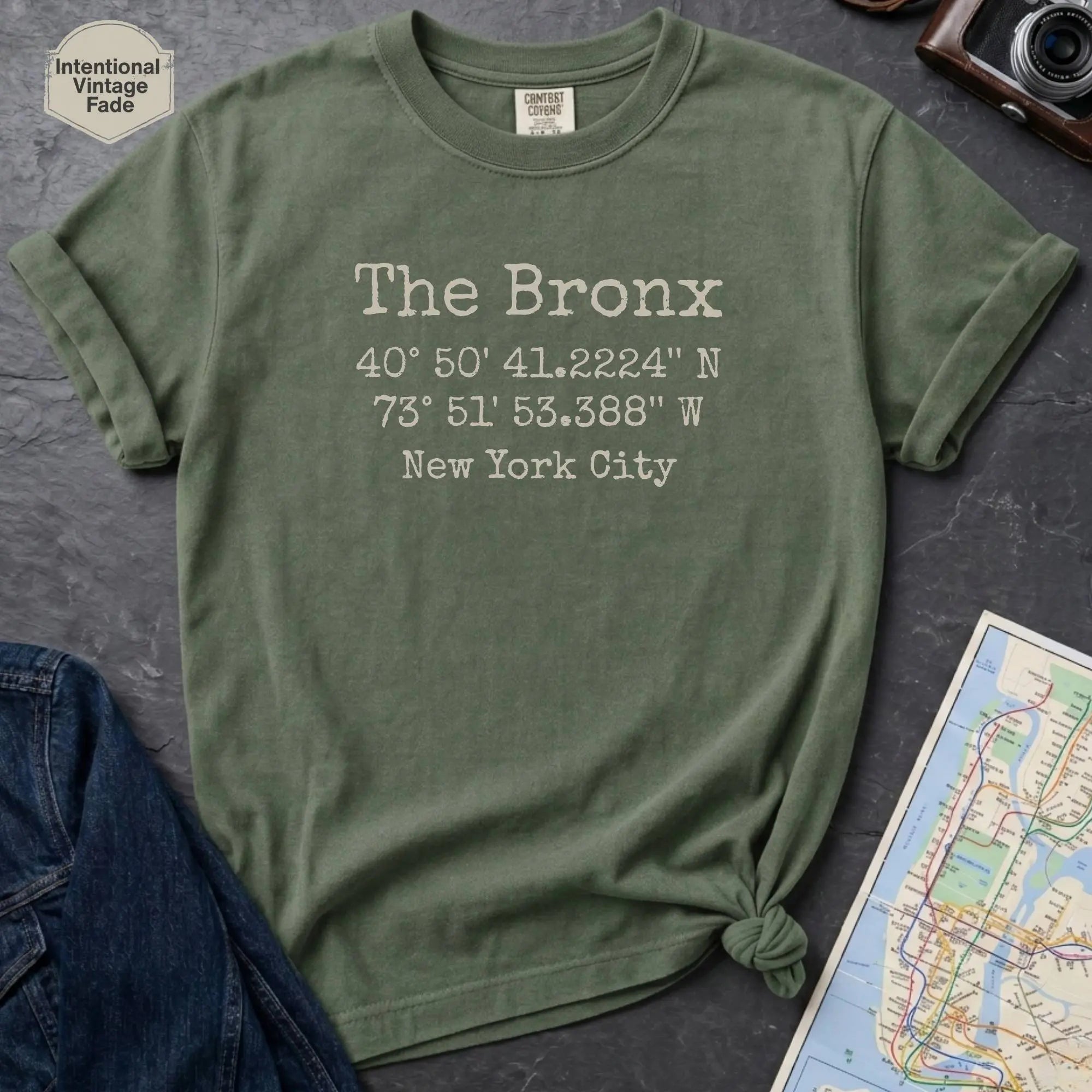 Moss green Comfort Colors t-shirt featuring The Bronx, NY coordinates and New York City text in a minimalist typewriter-style design.
