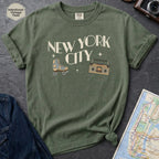 Moss green t-shirt with 'New York City' text and a roller skate and boom box on a dark surface with a map and camera.