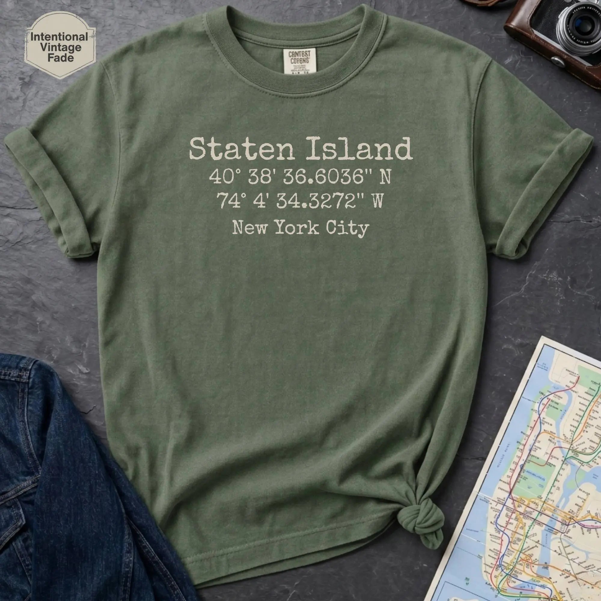 Moss green Comfort Colors t-shirt featuring a minimalist Staten Island coordinates design with “Staten Island,” latitude and longitude, and “New York City” printed in a vintage-style font.