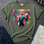 Moss green t-shirt with a graphic of a person spray painting a colorful mural on a brick wall.