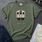 Moss Green t-shirt with a NYC subway train graphic on a dark surface with a map and a denim jacket.