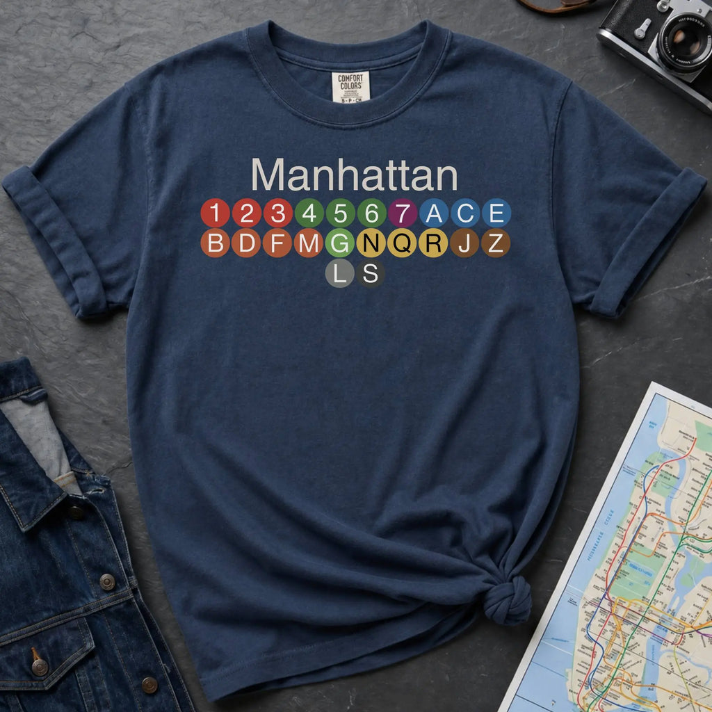 Navy Comfort Colors t-shirt featuring a minimalist Manhattan subway line graphic with colorful NYC train icons.