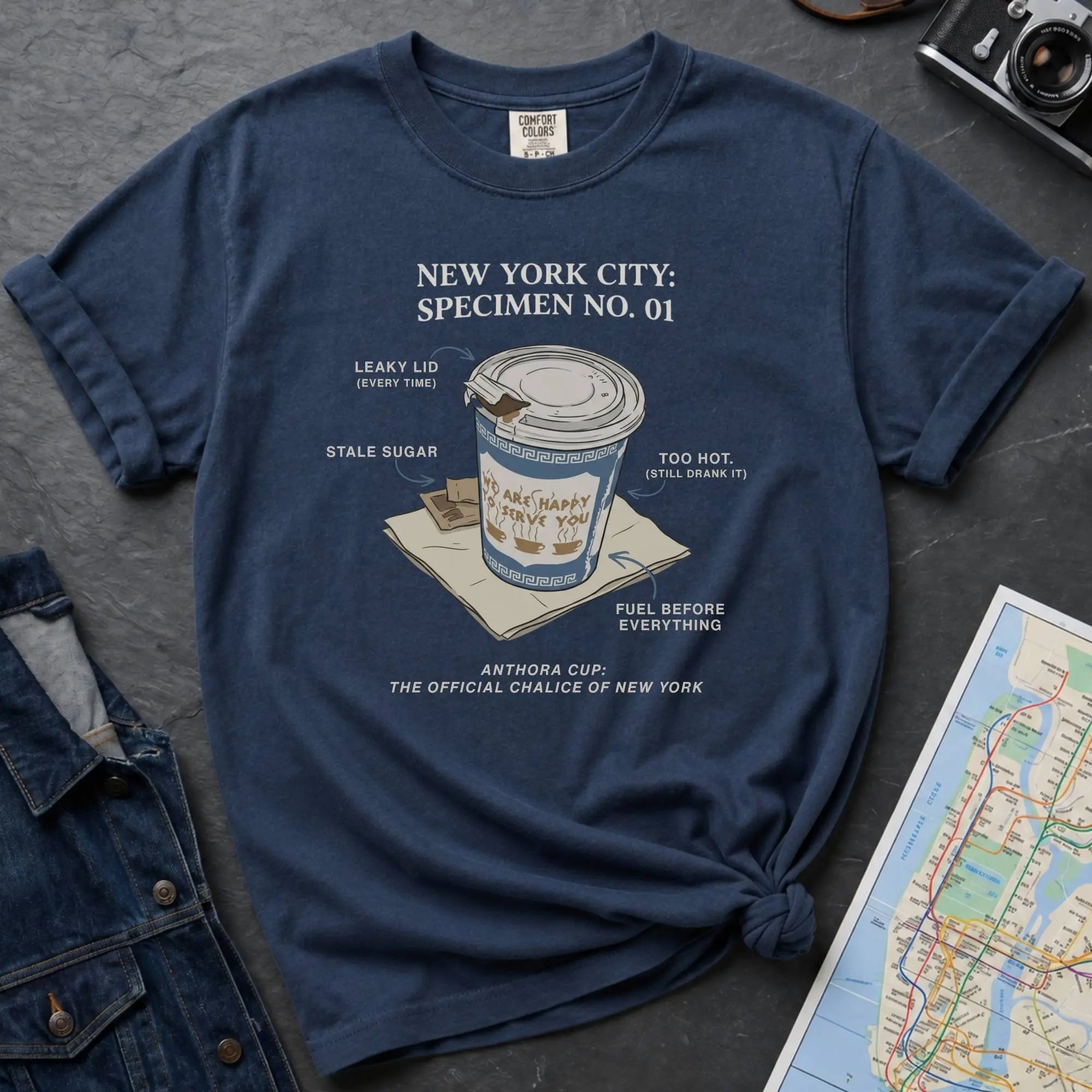 Navy t-shirt with New York City coffee cup graphic on a textured surface with map and camera.