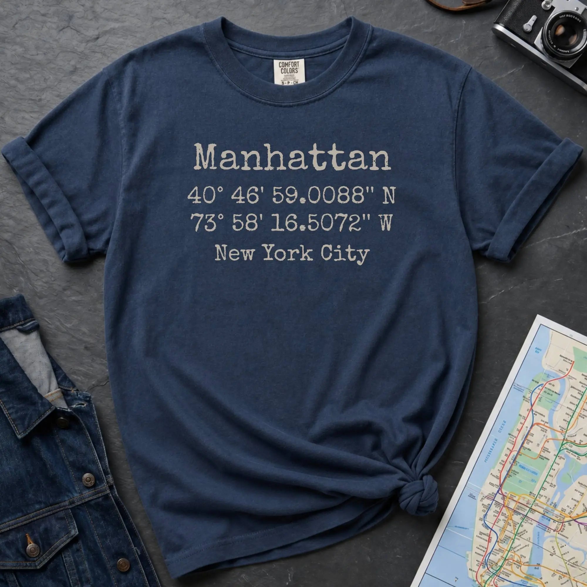 Navy Comfort Colors t-shirt featuring Manhattan, NY coordinates and New York City text in a minimalist typewriter-style design.