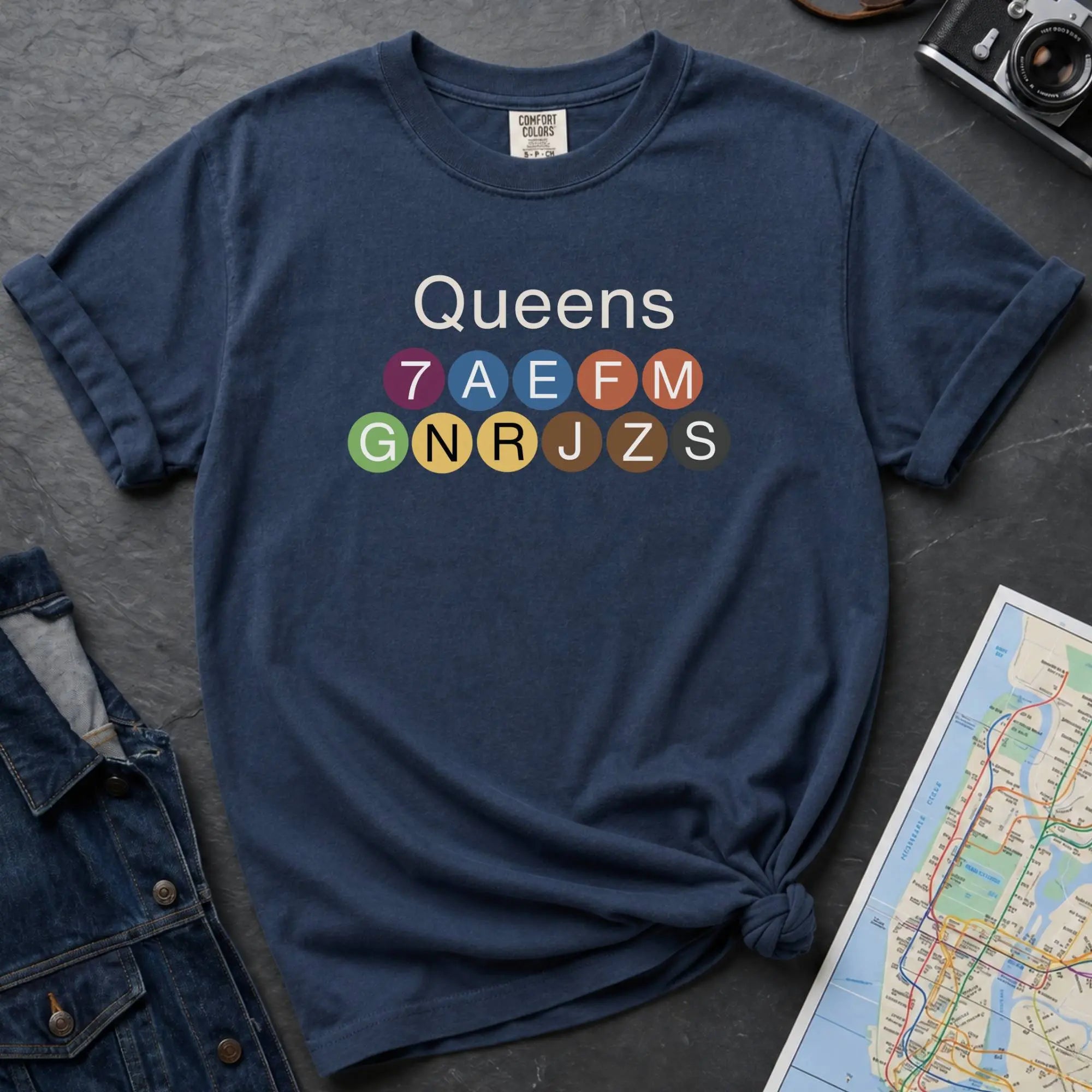 Navy Black Comfort Colors t-shirt featuring a minimalist Queens subway line graphic with colorful NYC train icons.