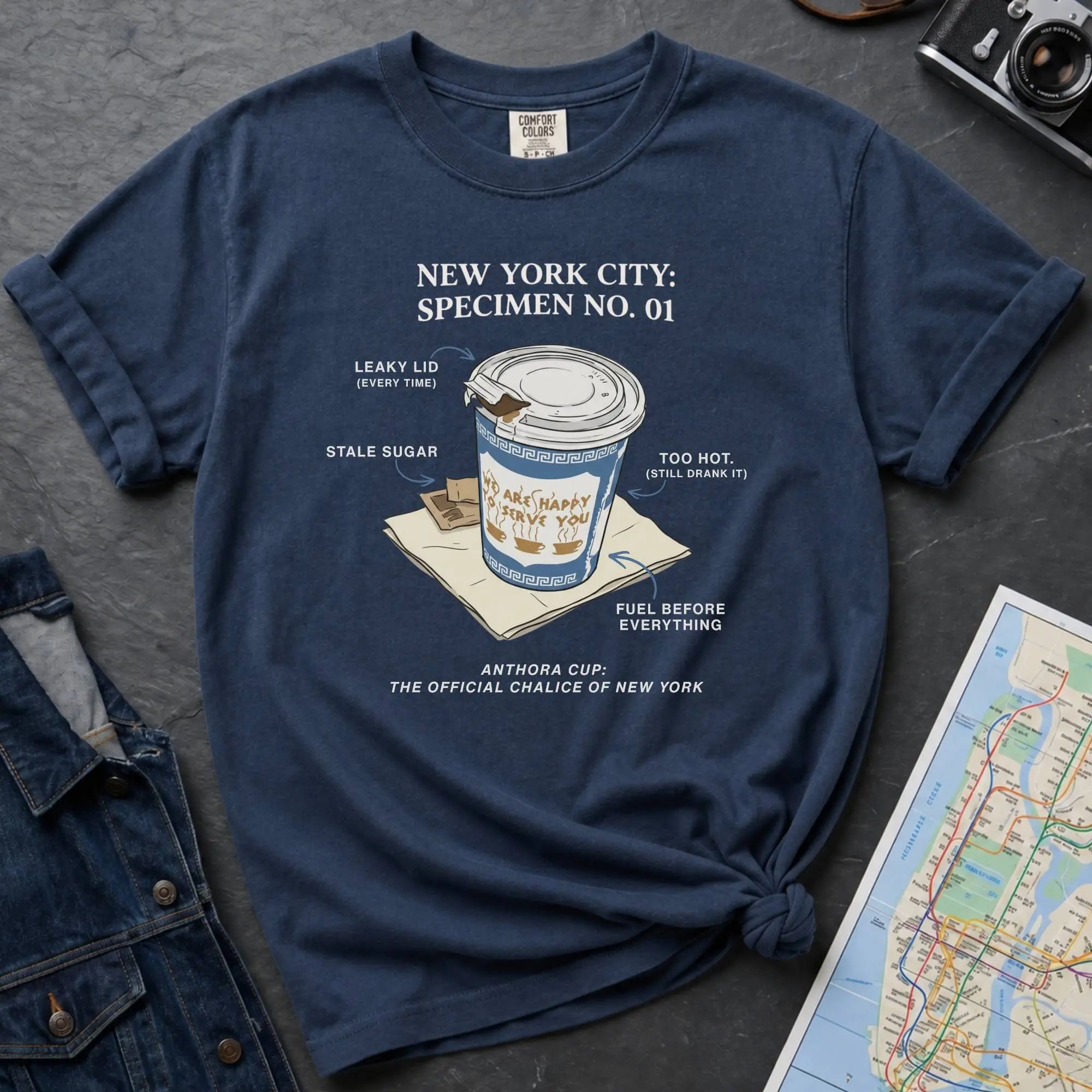 Navy t-shirt with New York City coffee cup graphic on a textured surface with map and camera.