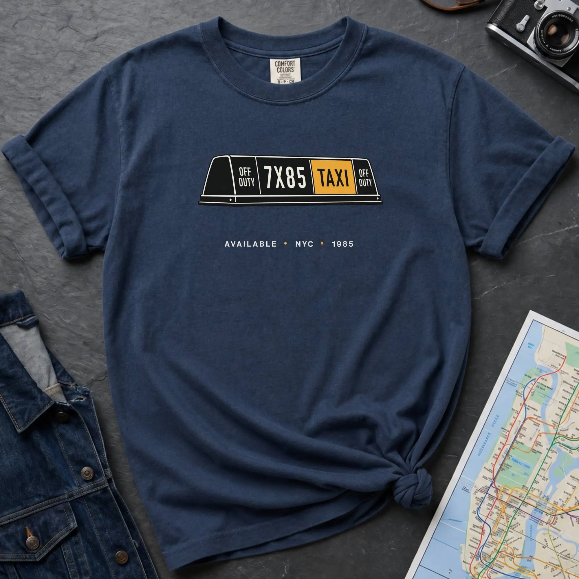 Navy Comfort Colors t-shirt featuring a vintage New York City taxi roof sign graphic with “Available • NYC • 1985” text.
