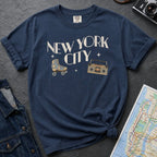 Navy t-shirt with 'New York City' text and a roller skate and boom box on a dark surface with a map and camera.