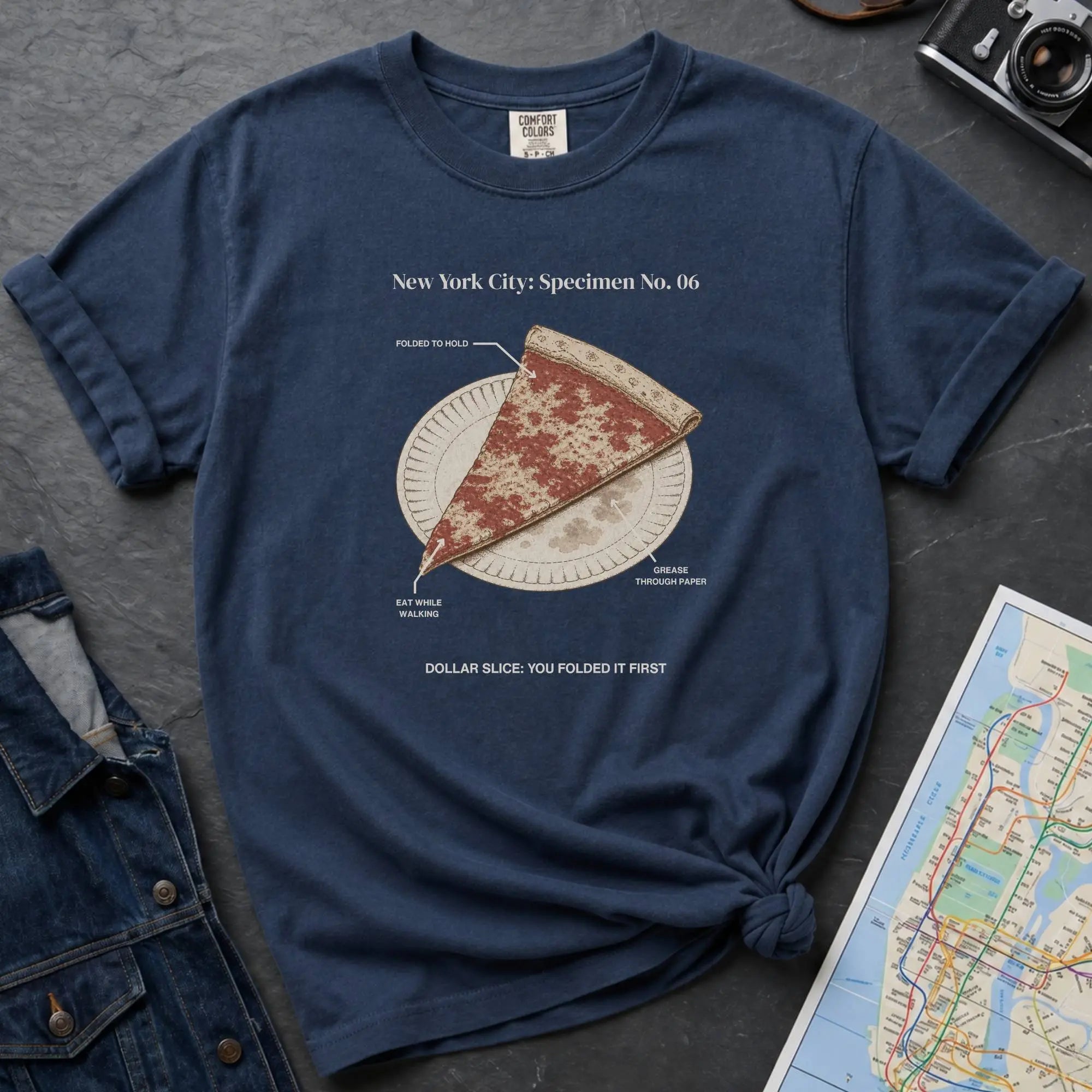 Navy Comfort Colors t-shirt featuring a vintage New York City dollar slice pizza graphic with specimen-style callouts and a folded slice on a paper plate.