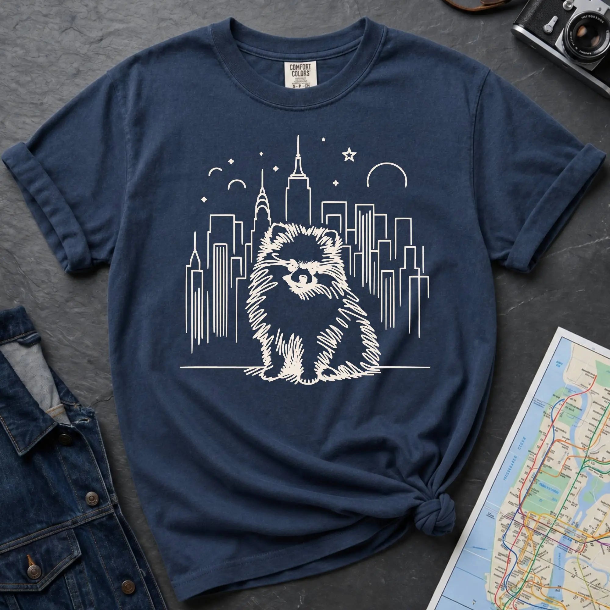 Navy Comfort Colors t-shirt featuring a fluffy small dog illustration in front of the New York City skyline.
