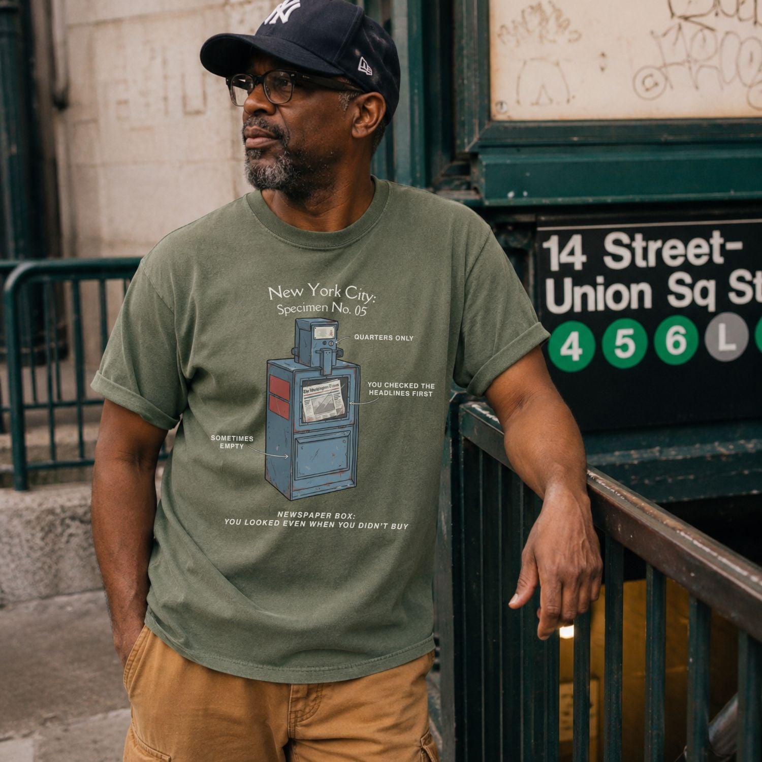 A man wearing a Moss green t-shirt with a newspaper box graphic and text