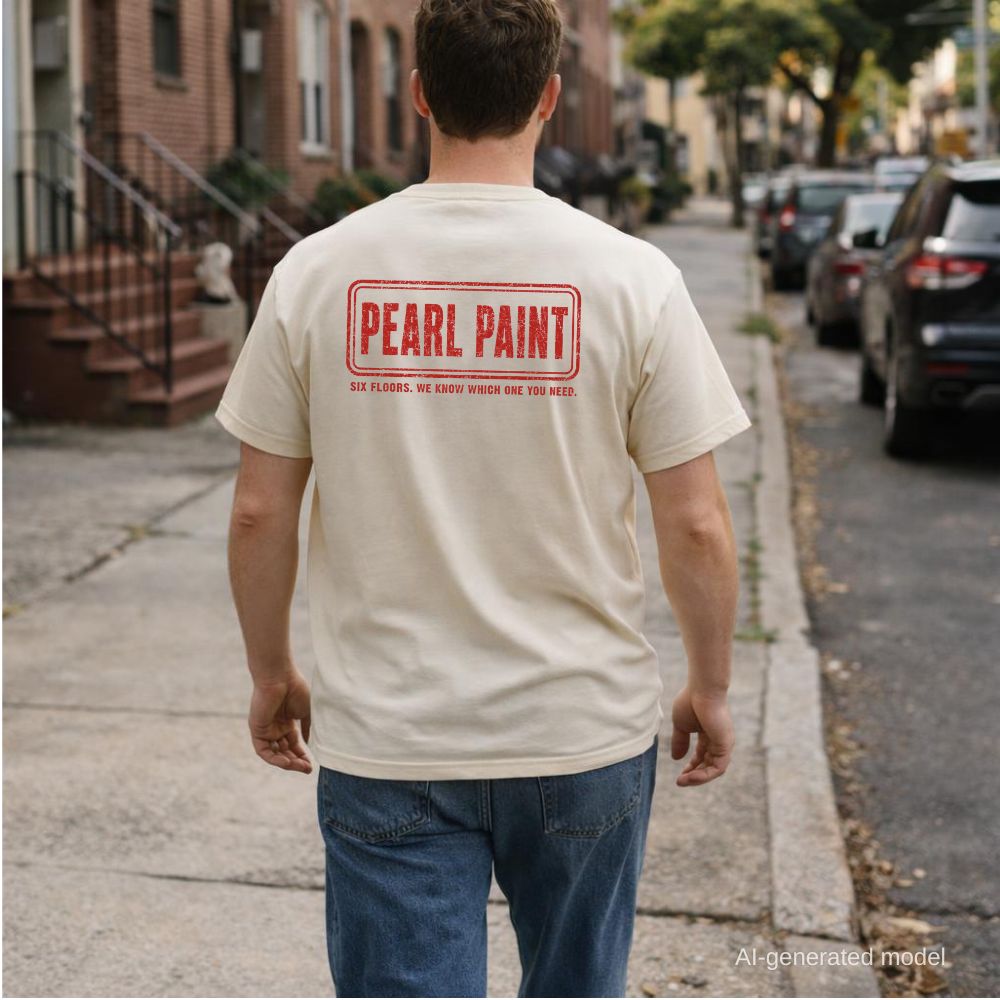 A man wearing an ivory Comfort Colors T-shirt with red Pearl Paint NYC back print as he walks down a city street.
